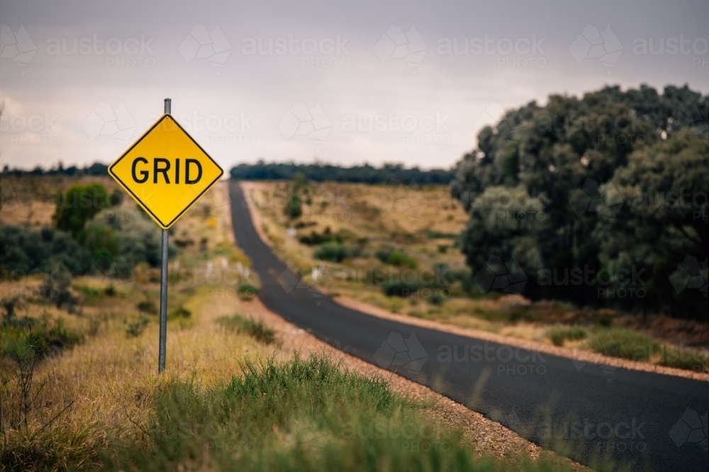 A yellow diamond-shaped road sign with the word “GRID” placed on the left side of a two-lane road - Australian Stock Image