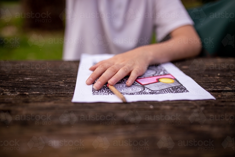 A young Aboriginal girl's hand resting on a drawing of the Aboriginal flag on a table - Australian Stock Image