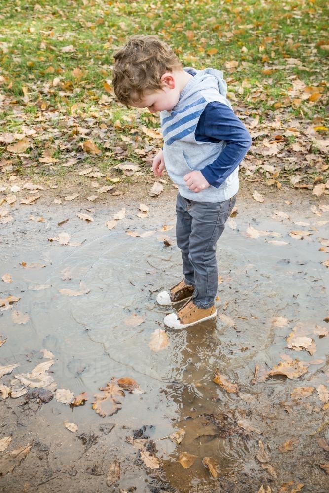 A young boy jumping in a puddle of water - Australian Stock Image