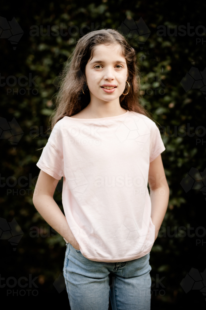 A young caucasian girl poses in front of a green hedge on a sunny evening in Australia - Australian Stock Image