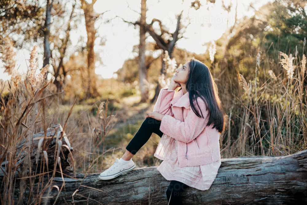 A young girl sitting on a fallen log looking up at the sky - Australian Stock Image