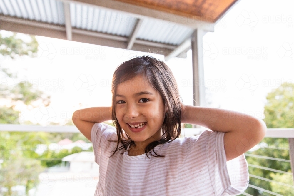 A young girl smiling at the camera with her hands at the back of her head - Australian Stock Image