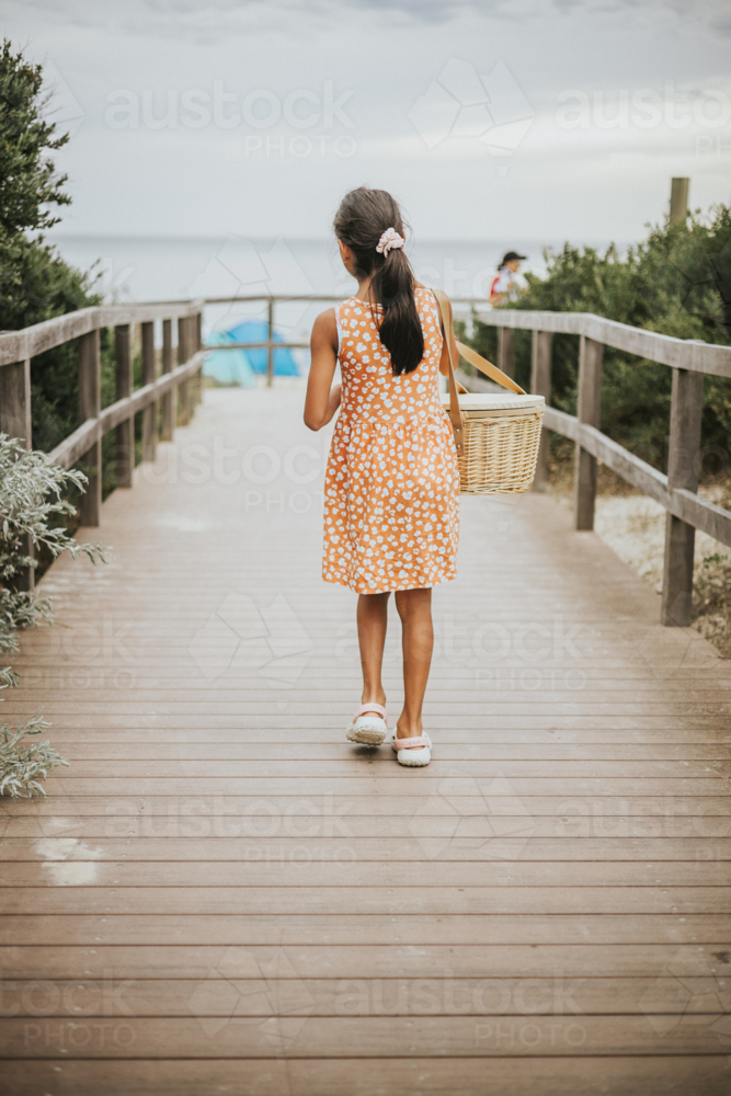 A young girl walking to the beach carrying a picnic basket - Australian Stock Image
