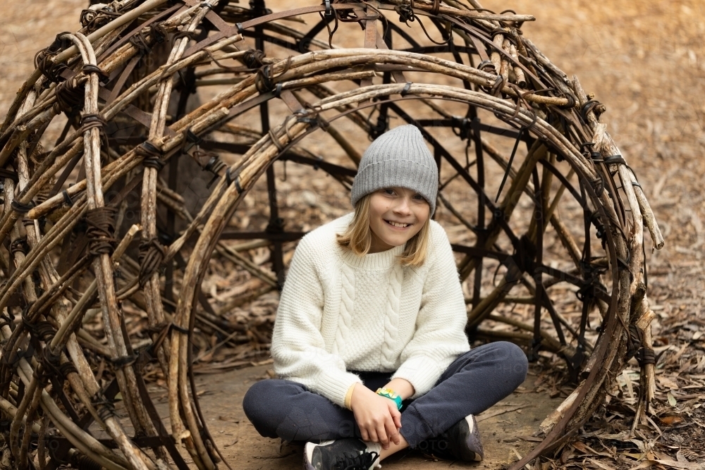 A young girl wearing a grey beanie sitting in a woven basket in a children's playground - Australian Stock Image