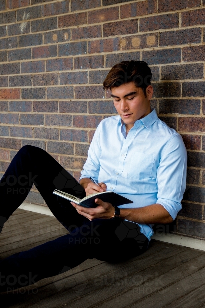 A young male sitting on the ground on a covered verandah - Australian Stock Image