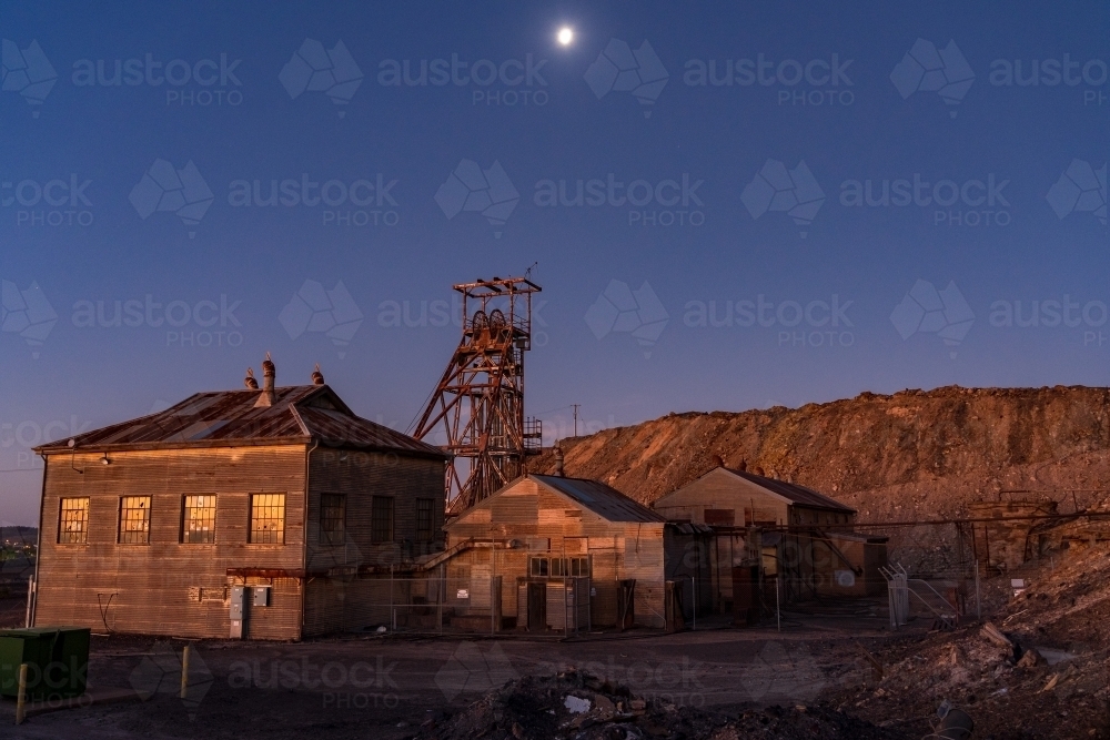 Abandoned sheds and poppet head in a mining landscape under full moon - Australian Stock Image