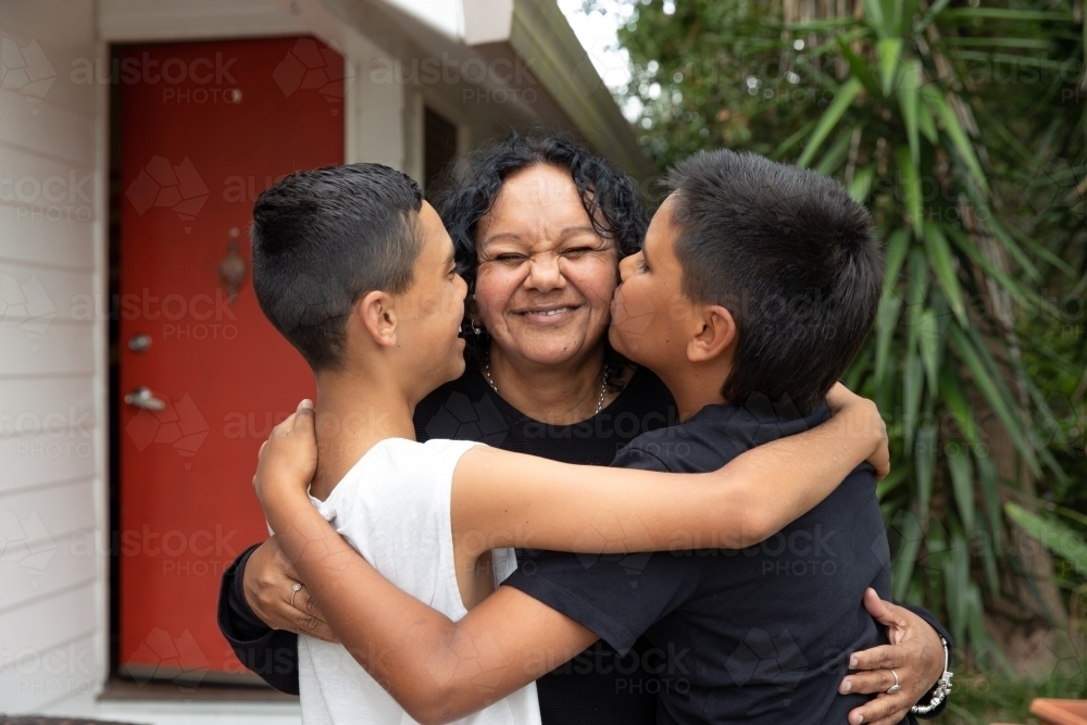 Aboriginal family hugging and kissing in backyard - Australian Stock Image