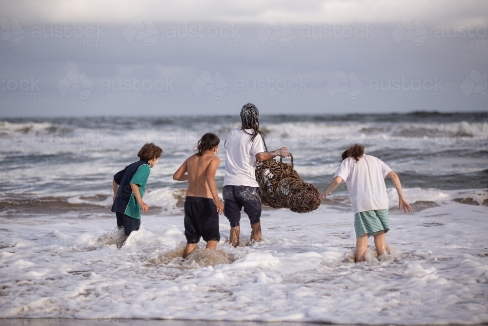 Aboriginal family playing in waves at a beach with fish trap - Australian Stock Image