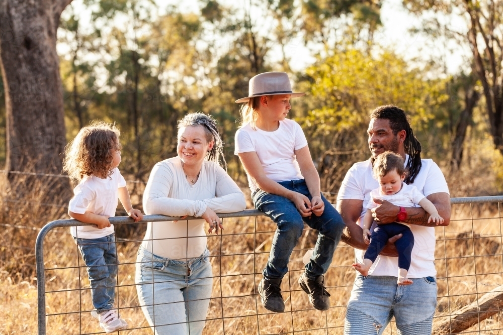 Aboriginal family portrait on farm paddock gate with parents and children - Australian Stock Image