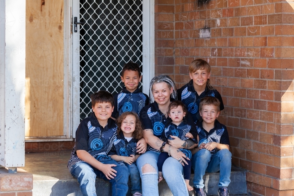 Aboriginal family sitting together on front doorstep - mum with her six kids - Australian Stock Image