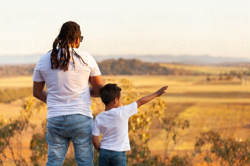 Aboriginal father and son looking out over golden Australian landscape - Australian Stock Image