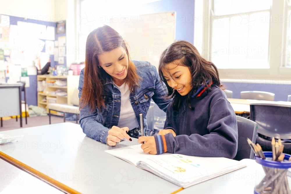 Aboriginal female school teacher sitting with her student in the classroom - Australian Stock Image