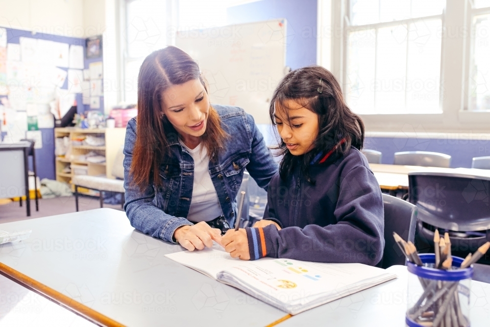 Aboriginal female school teacher sitting with her student in the classroom - Australian Stock Image