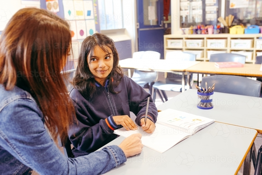 Aboriginal female school teacher sitting with her student in the classroom - Australian Stock Image