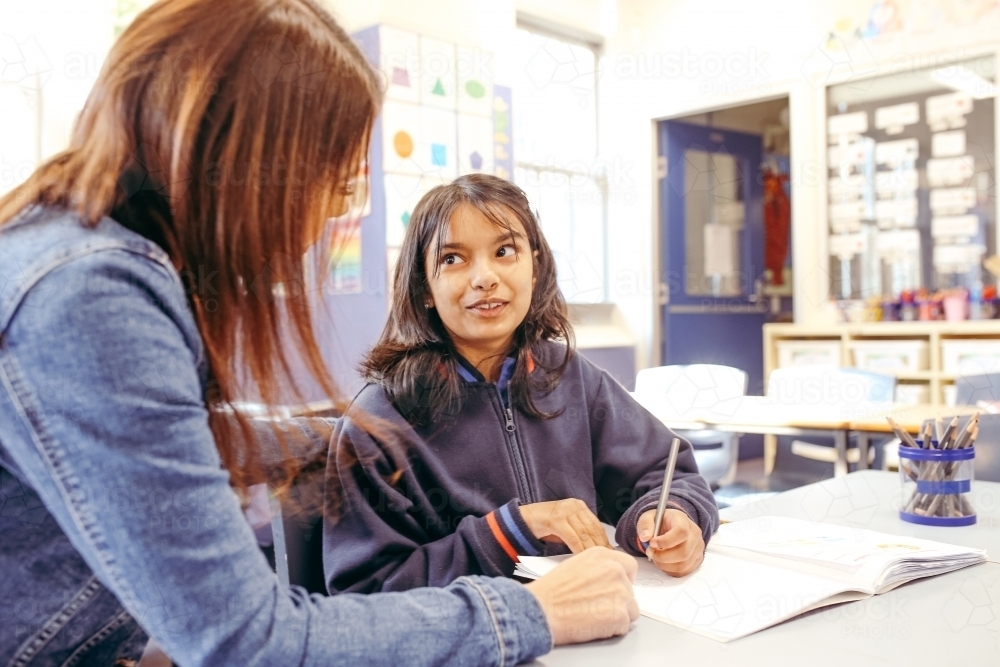 Aboriginal female school teacher sitting with her student in the classroom - Australian Stock Image