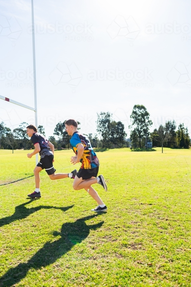 Aboriginal football players running on sports ground field in game - Australian Stock Image