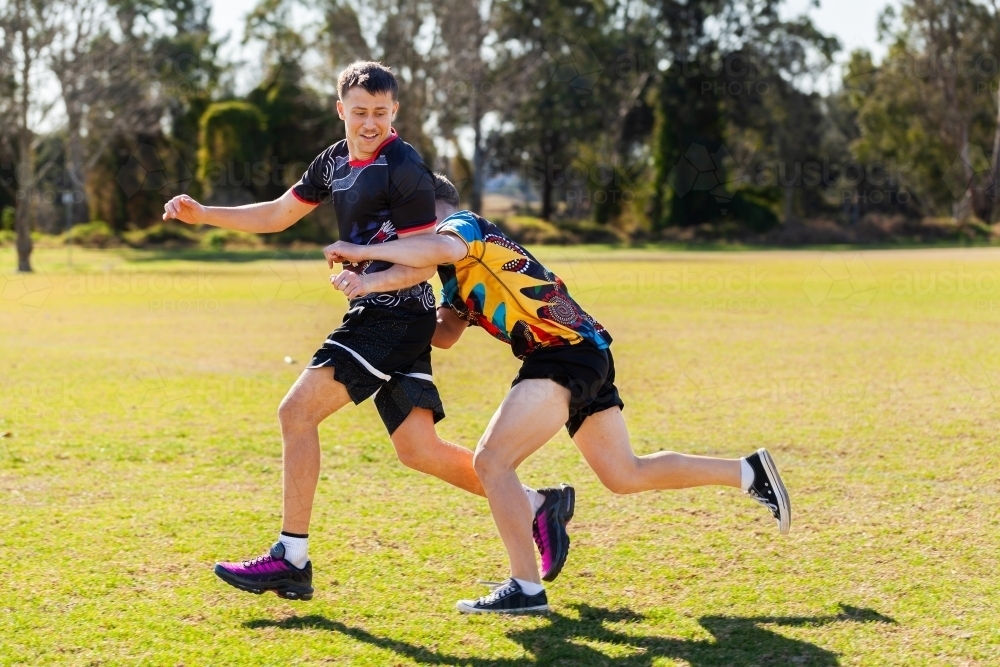 Aboriginal football players running on sports ground field tackling during game - Australian Stock Image