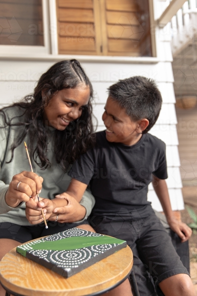 Aboriginal girl and boy dot painting together - Australian Stock Image