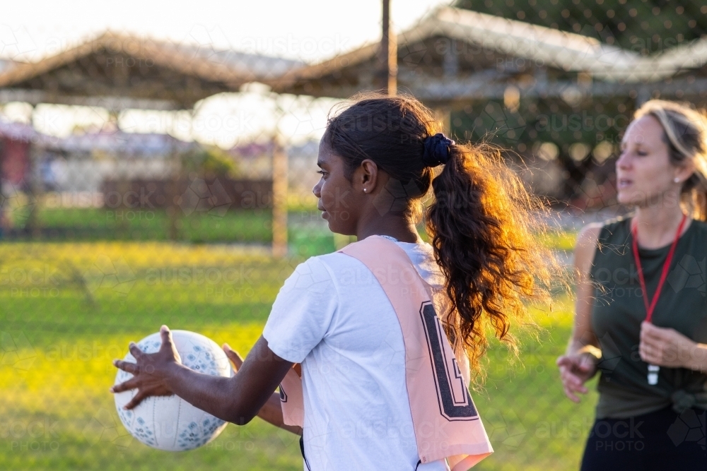 aboriginal girl catching netball with Caucasian umpire or coach in background - Australian Stock Image