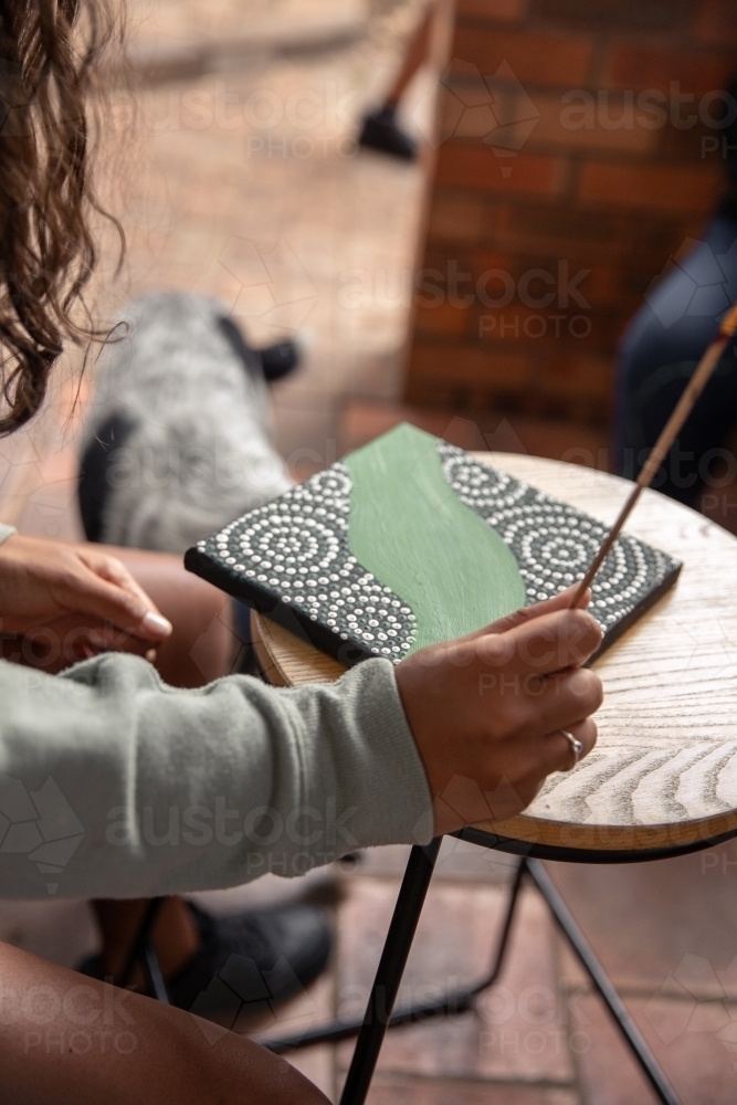 Aboriginal girl dot painting on a stool - Australian Stock Image