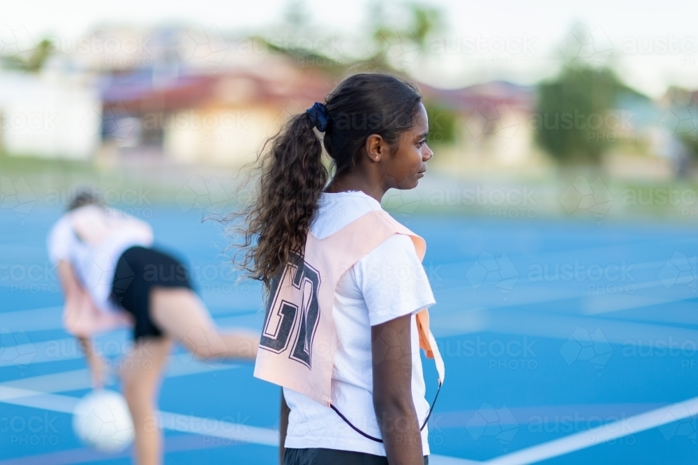 aboriginal girl facing away with blurry background of netball court - Australian Stock Image