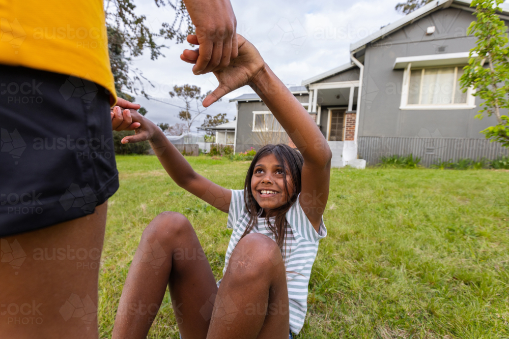 aboriginal girl holding hands to stand up on lawn outside house - Australian Stock Image