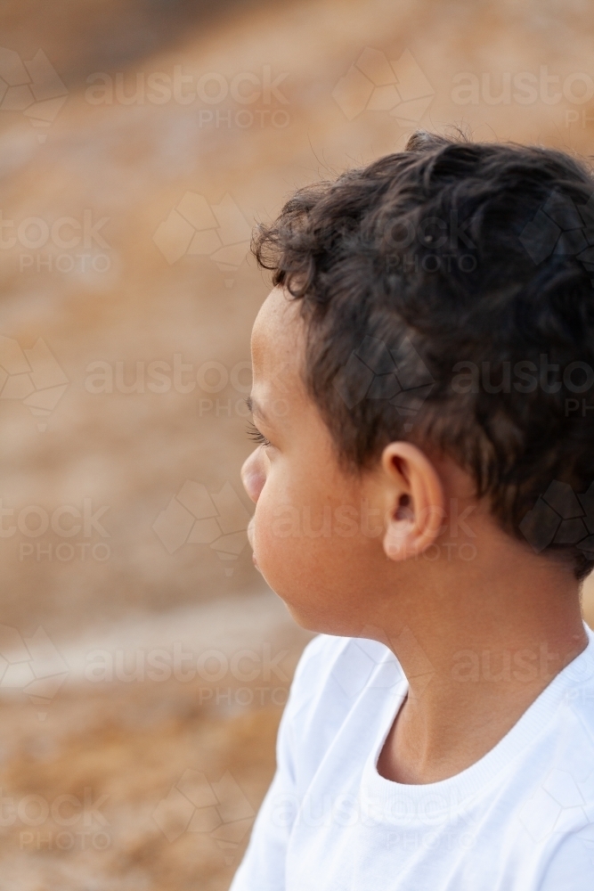 Aboriginal kid looking away sitting outside on country - Australian Stock Image