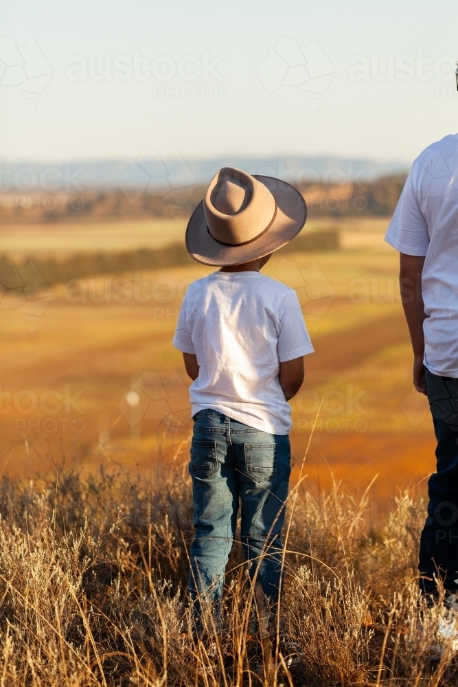 Aboriginal kid standing on cliff looking out over australian landscape - Australian Stock Image