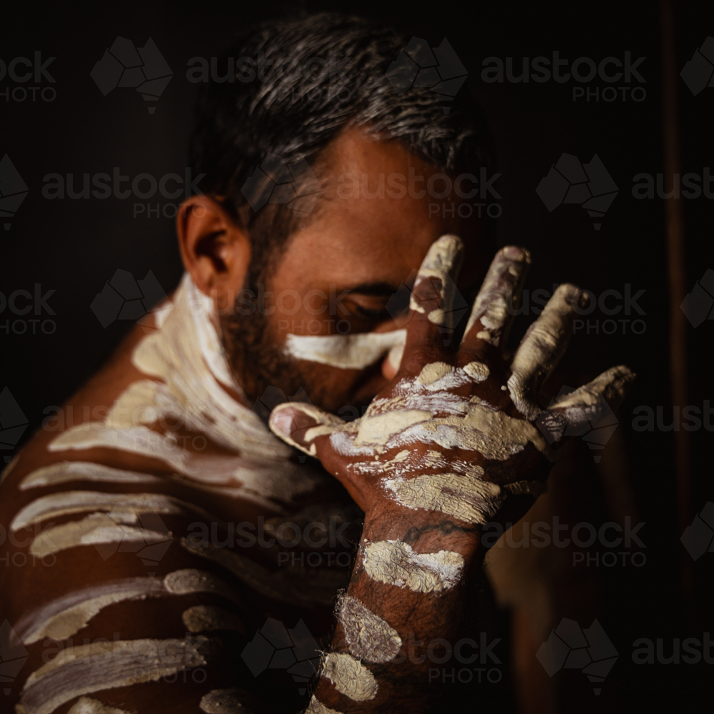 Aboriginal male painted up covering face - Australian Stock Image