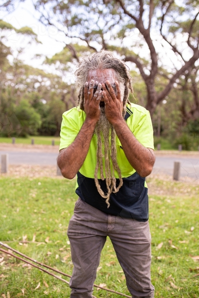 Aboriginal man applying white face paint to his face - Australian Stock Image