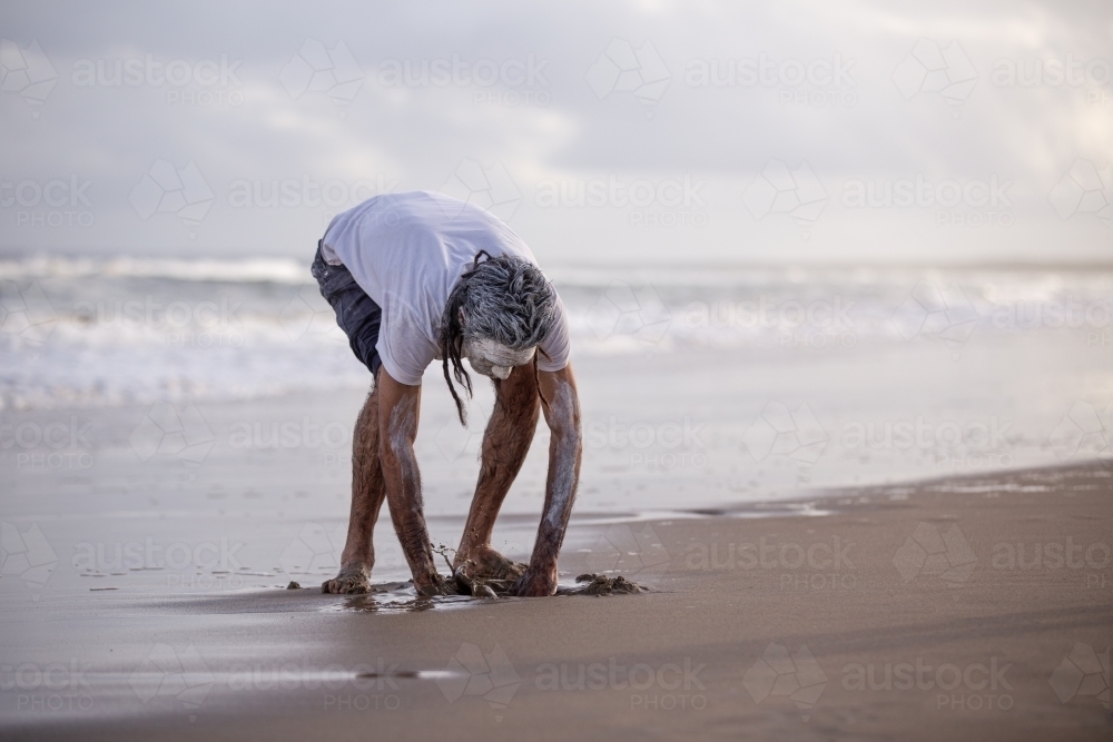 Aboriginal man digging with his hands on a beach - Australian Stock Image