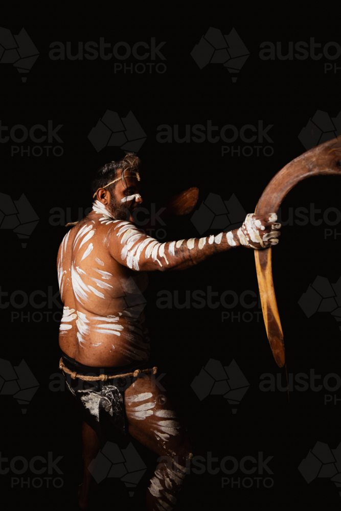 Aboriginal man holding a pair of boomerangs in a dark background. - Australian Stock Image
