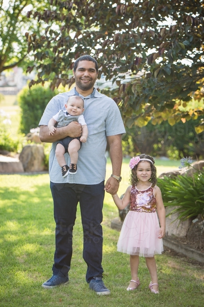 Aboriginal man holding baby son and holding daughter's hand - Australian Stock Image