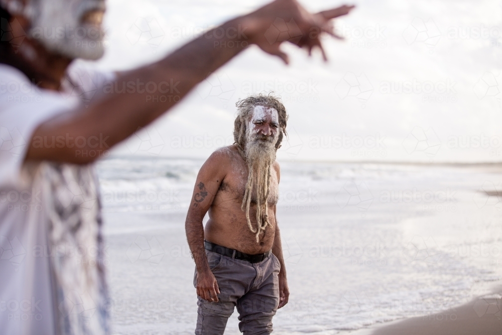 Aboriginal man looking at another Aboriginal man speaking standing on a beach - Australian Stock Image