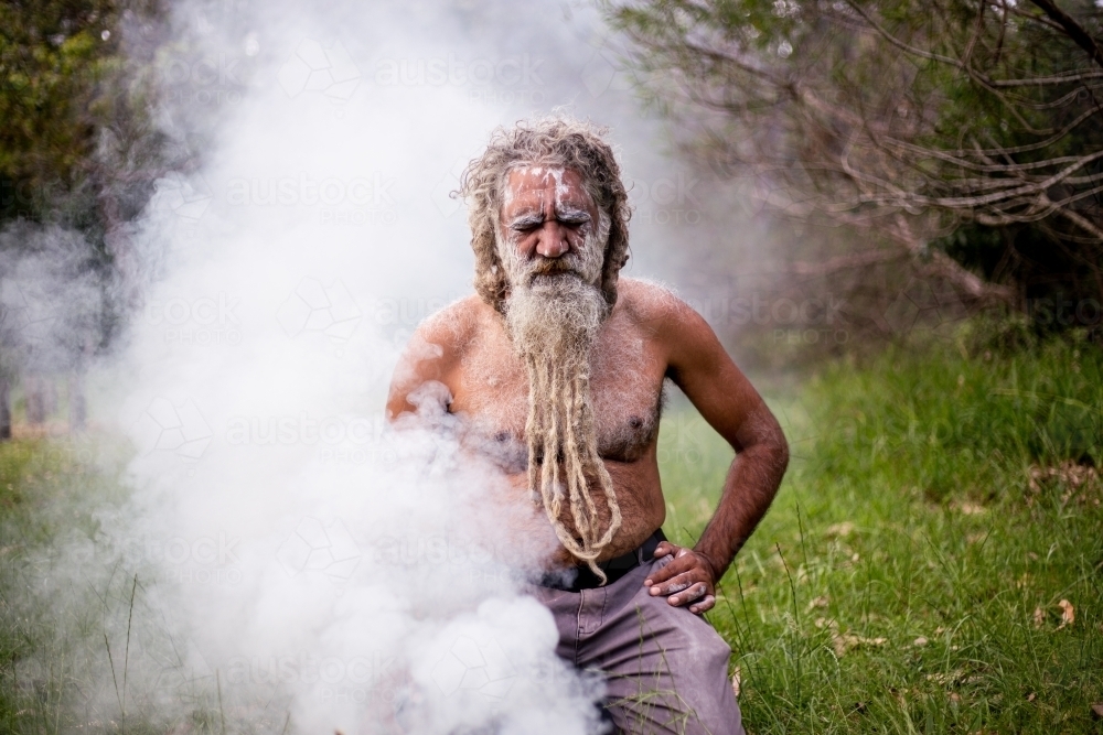 Aboriginal man sitting in smoke at a smoking ceremony - Australian Stock Image