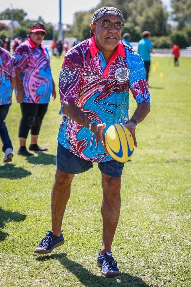 Aboriginal man wearing glasses passing a football - Australian Stock Image