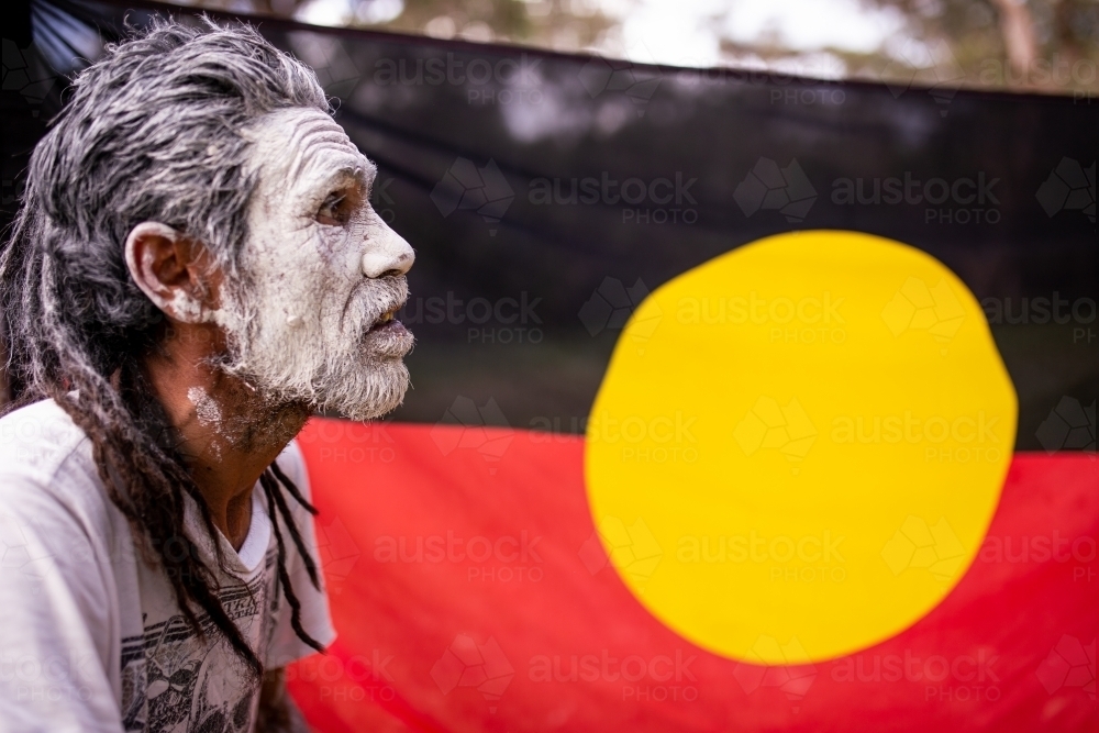 Aboriginal man wearing white face paint in front of the Aboriginal flag - Australian Stock Image