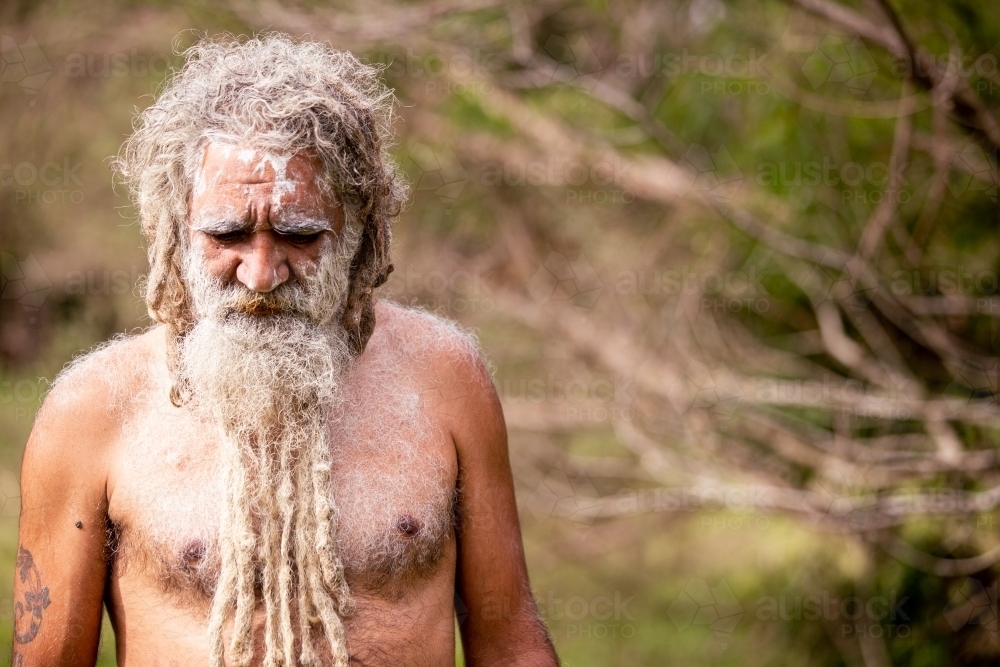 Aboriginal man wearing white face paint looking at the ground - Australian Stock Image