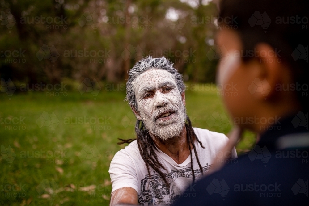 Aboriginal man wearing white face paint talking to a young Aboriginal boy - Australian Stock Image