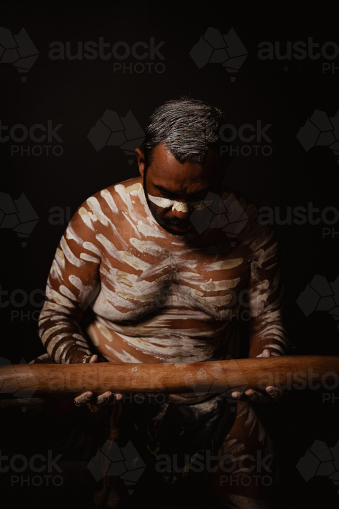 Aboriginal man with white body paint holding a wooden didgeridoo. - Australian Stock Image