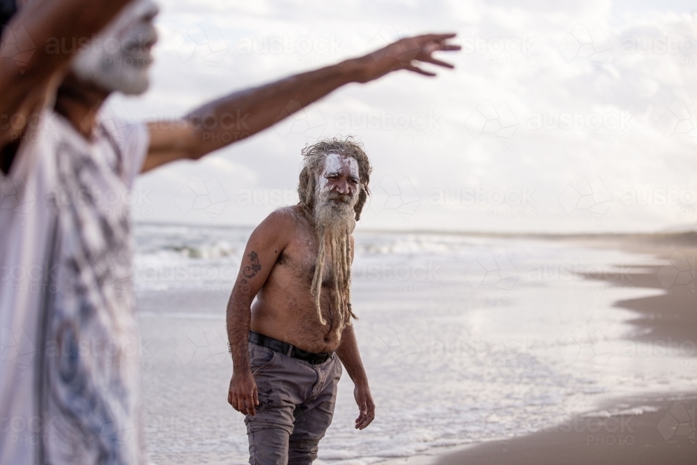 Aboriginal middle aged man listening to another Aboriginal man talking on a beach - Australian Stock Image