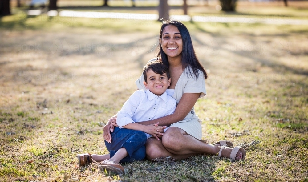 Aboriginal mother sitting with arms around mixed race aboriginal and caucasian son - Australian Stock Image