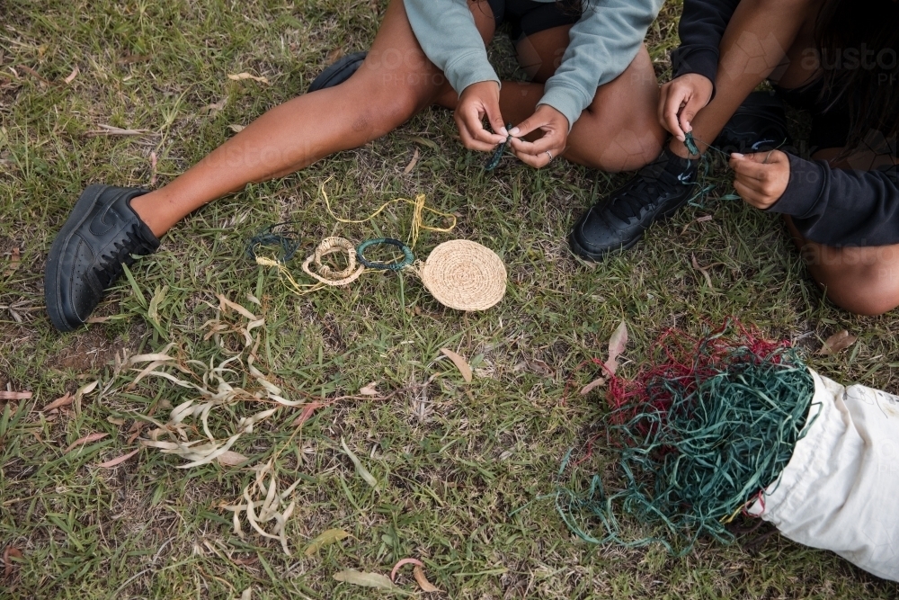 Aboriginal people sitting on grass, basket weaving together - Australian Stock Image