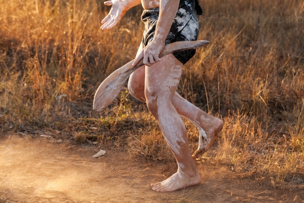 Aboriginal person dancing and telling cultural stories while holding digging and hunting stick - Australian Stock Image