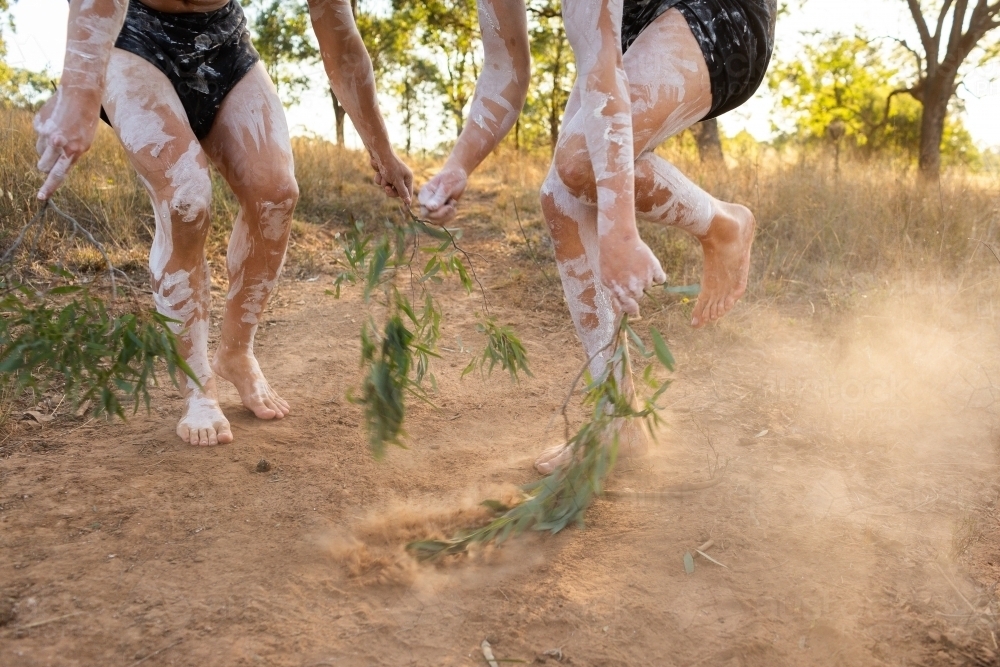 Aboriginal storytelling dance with gum leaves in dancers hands flicking up soft dust on country - Australian Stock Image