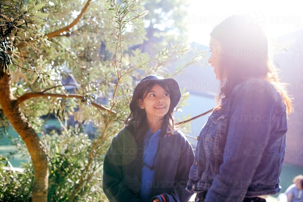 Aboriginal teacher talking to her female student outside in the school playground - Australian Stock Image