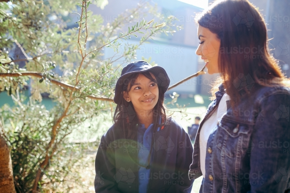 Aboriginal teacher talking to her female student outside in the school playground - Australian Stock Image