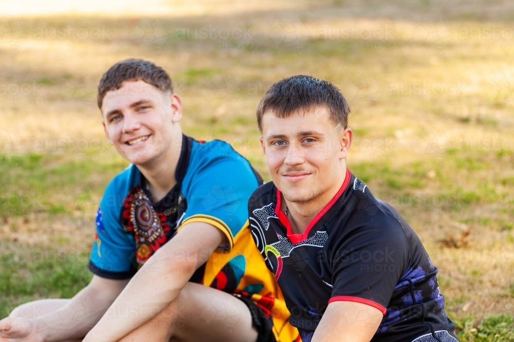 Aboriginal teen sport players sitting on side-lines of footy field - Australian Stock Image