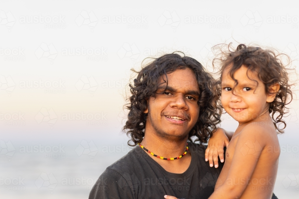 aboriginal teenager holding young sibling against pale sky - Australian Stock Image