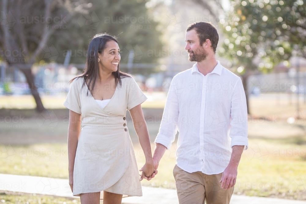 Aboriginal woman holding hands with caucasian man looking at each other - Australian Stock Image